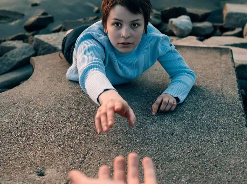 Woman laying on a rock holding out her hand for someone else