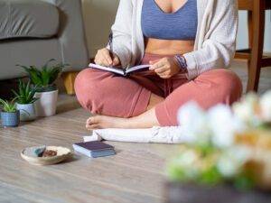 Woman in yoga clothes sitting down writing manifestations in a book
