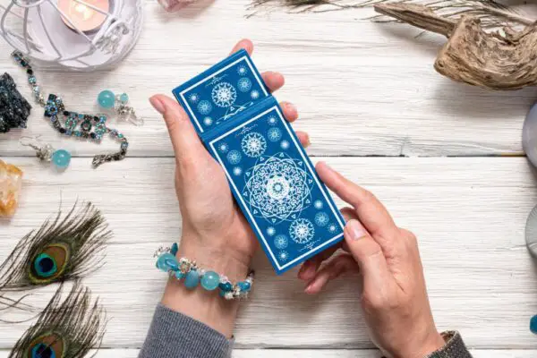 Hand holding blue deck of tarot cards on light wood table
