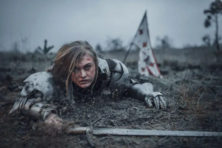 Girl in image of Jeanne d'Arc in armor crawls in mud with sword